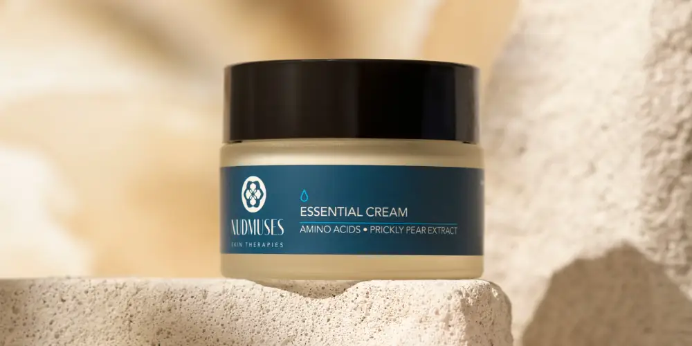 Nudmuses Essential Cream umieszczony na kamieniu, na neutralnym, beżowym tle.