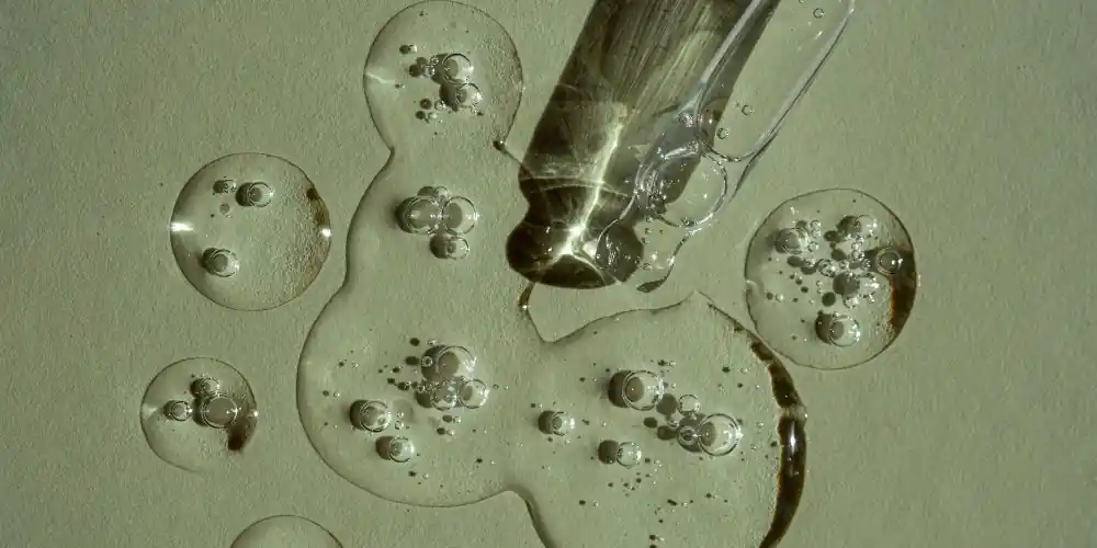 Transparent serum spilling from a glass pipette onto a light green background