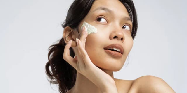 A woman applying cream to her face.